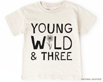 May include: A light beige t-shirt with black text that reads "Young Wild & Three" and a small black and white flower graphic.
