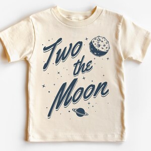 May include: A cream colored t-shirt with a blue graphic that says "Two the Moon" with a crescent moon and a planet graphic.