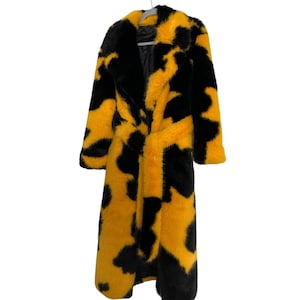 Puede incluir: Abrigo largo de piel sintética con un llamativo estampado en negro y amarillo. El abrigo presenta un cuello chal, un cinturón anudado y un diseño hasta la rodilla. El abrigo está colgado de una percha sobre un fondo blanco.