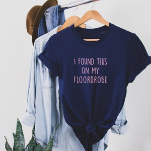 Puede incluir: Una camiseta azul marino con el texto "I found this on my floordrobe" en letras rosas.