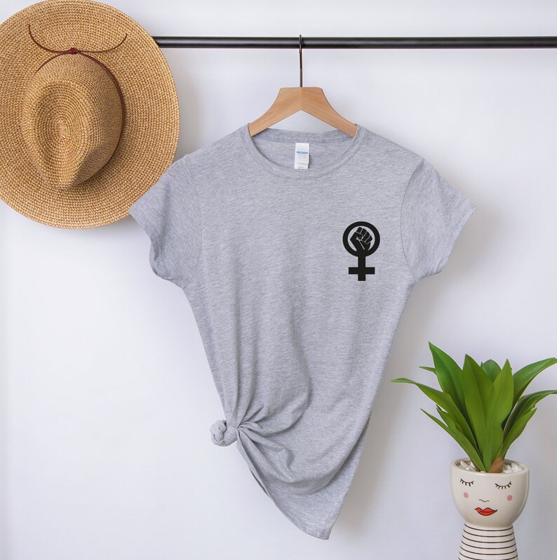 Puede incluir: Una camiseta gris con un s&iacute;mbolo feminista negro con un pu&ntilde;o levantado dentro del c&iacute;rculo.