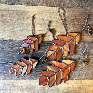 May include: Five stained glass oak leaf ornaments with copper chains and acorn accents. The leaves are in shades of brown, orange, and red.