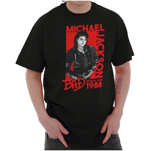 May include: Black t-shirt featuring a red graphic of Michael Jackson with the text "MICHAEL JACKSON" and "BAD WORLD TOUR 1988". The image shows a portrait of Michael Jackson in a black leather jacket.