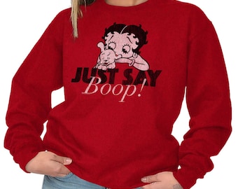 Op de afbeelding: Rode longsleeve met een afbeelding van Betty Boop en haar hond. De tekst "Just Say Boop!" is in zwart onder de afbeelding gedrukt.