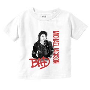 May include: White t-shirt featuring a black and white image of Michael Jackson. The words "MICHAEL JACKSON" are printed vertically in red, with "BAD" in red below the image. The shirt is a short-sleeved style.