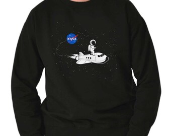 May include: Black sweatshirt with a white spaceship and astronaut graphic. The spaceship has a NASA logo on the side. The astronaut is wearing a white spacesuit and is holding onto the spaceship.
