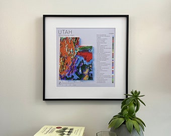 May include: A framed print of a geological map of Utah with a color-coded legend. The map shows the different rock formations and geological features of the state. The print is hanging on a white wall above a wooden table with books and a candle.