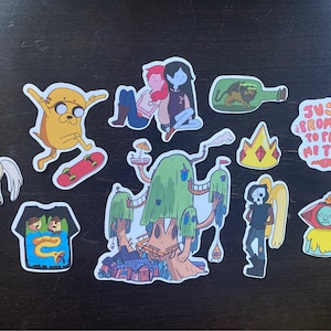 May include: A set of nine Adventure Time themed stickers featuring characters like Finn, Jake, and Princess Bubblegum. The stickers are printed on white paper with a glossy finish. The stickers are perfect for decorating laptops, water bottles, and other surfaces.