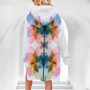 Pode incluir: Casaco branco com capuz com um design floral simétrico em tons de rosa, laranja, azul e verde. O casaco tem mangas compridas e um corte ao joelho. O padrão floral é uma característica marcante nas costas.