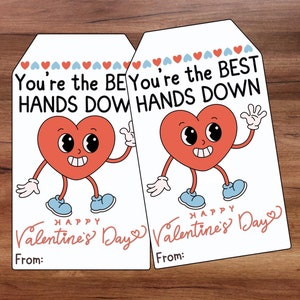 May include: Two white Valentine's Day gift tags with a red heart character wearing blue shoes. The text on the tags reads "You're the BEST HANDS DOWN" and "Happy Valentine's Day".
