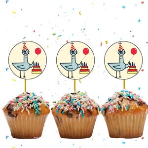 May include: Three cupcakes topped with colorful sprinkles and decorative toppers. The toppers feature a cartoon pigeon holding a red balloon and a birthday cake. Confetti is scattered around the cupcakes.