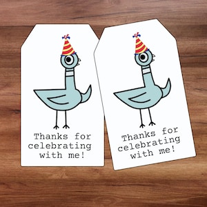 May include: Two white gift tags featuring a cartoon pigeon wearing a party hat. The pigeon is light blue with black outlines. Text on the tags reads "Thanks for celebrating with me!" on a wooden surface.