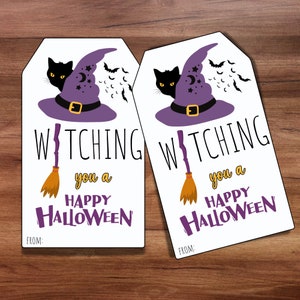 Op de afbeelding: Twee witte cadeau-etiketten met een zwarte kat die uit een paarse heksenhoed kijkt. De tekst op de etiketten luidt "Witching you a Happy Halloween" met een bezem en oranje sterren. Er is ruimte voor "From:" onderaan elk etiket.