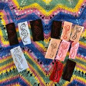 May include: A collection of fabric patches with hand-printed designs. The designs include a snake wearing a cowboy hat and a mushroom. The patches are in various colors, including red, black, white, and pink.