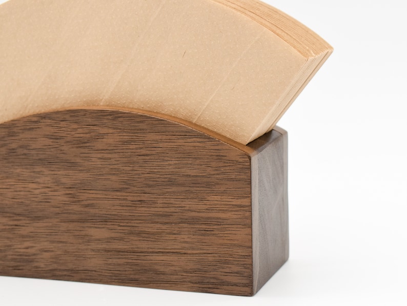 May include: A wooden coffee filter holder with a stack of brown paper coffee filters inside. The holder is made of dark wood with a natural grain pattern.