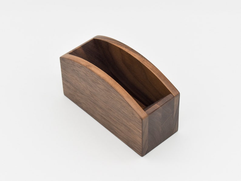 May include: A wooden coffee filter holder with a curved top and a rectangular base. The holder is made of dark brown wood.