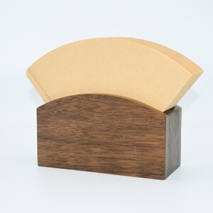 May include: A wooden coffee filter holder with a brown paper filter inside. The holder is made of dark wood with a natural grain pattern.