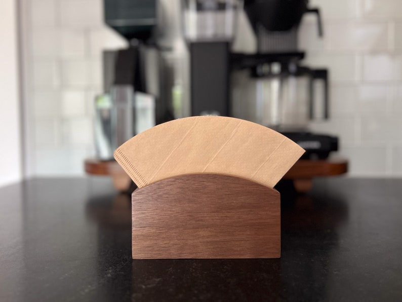 May include: A wooden coffee filter holder with a brown paper filter inside. The holder is made of dark wood and has a curved shape.