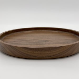 May include: A round wooden tray made of walnut wood. The tray has a slightly raised edge and a smooth, polished surface.