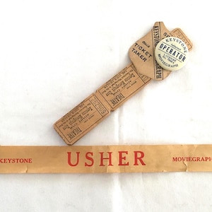 May include: Vintage movie theater ephemera, including a ticket stub, a "Ticket Taker" card, and an "Operator" pin. The ticket stub is tan with black text and the number 262909. The "Usher" sign is tan with red text.