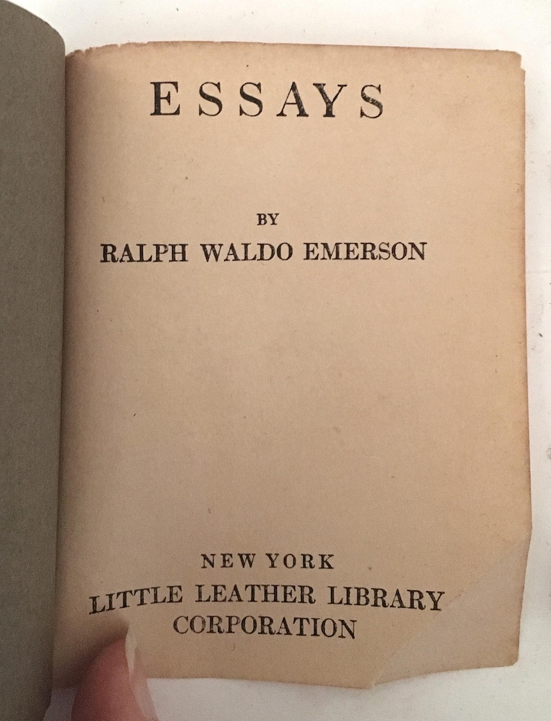 May include: Open book with the title "ESSAYS" at the top, followed by "BY RALPH WALDO EMERSON." Below, it reads "NEW YORK LITTLE LEATHER LIBRARY CORPORATION." The pages are aged with a tan color.