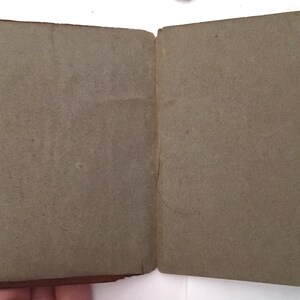 May include: An open, vintage book with aged, gray pages. The cover is a dark brown with visible wear and tear. The pages are slightly textured and show signs of age. The book is held open, revealing the interior pages.