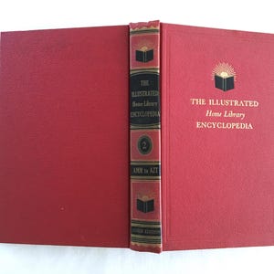 May include: An open, red hardcover book titled "The Illustrated Home Library Encyclopedia." The spine is dark red with gold lettering and a decorative design. The book is a "Guild Edition."