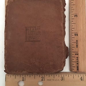 May include: A small, brown leather-bound book with the embossed text "LITTLE LEATHER LIBRARY." The book is approximately 3 inches long and 2 inches wide. The edges of the book are rough and worn, suggesting age.