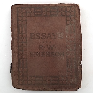 May include: A small, antique brown leather book titled "Essays" by R.W. Emerson. The cover features embossed decorative borders and lettering. The book shows signs of age and wear.