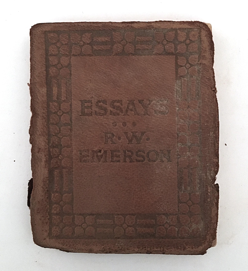 May include: A small, antique brown leather book titled "Essays" by R.W. Emerson. The cover features embossed decorative borders and lettering. The book shows signs of age and wear.