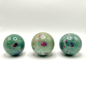 May include: Three green and pink ruby zoisite spheres. The spheres are smooth and polished.