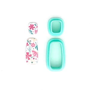 May include: Two floral nail art designs and two teal nail art molds are displayed on a white background. The nail art designs feature pink and white flowers. The molds are rectangular and square.