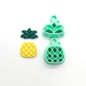 May include: A set of pineapple-shaped cookie cutters and a pineapple-shaped cookie. The cookie cutters are light green, and the cookie is yellow. The pineapple top is dark green.