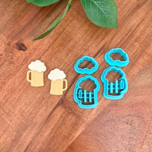 以下が含まれることがあります： ビールをテーマにしたクッキーカッターのコレクション。白い泡が付いたビールジョッキの形をした2つの黄色のクッキーカッターは、3つの青い雲の形をしたカッターと3つの青いビールジョッキのカッターの隣にあります。