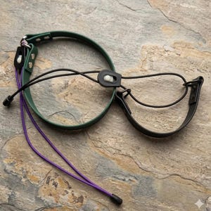 May include: A dark green circular collar and a black semi-circular collar connected by thin black elastic cords with white plastic toggles. A long purple cord with a black end cap is attached to the green collar with silver metal rivets.
