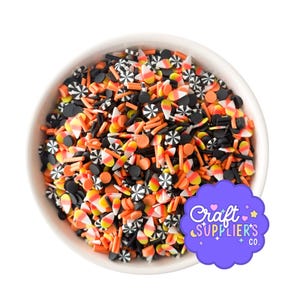 Op de afbeelding: Een witte kom gevuld met kleurrijke polymeerklei sprinkles. De sprinkles bevatten snoepmaïs, zwarte cirkels, oranje staafjes en zwart-witte windmolenvormen. Een paars logo met de tekst "Craft Supplier's Co." staat rechtsonder.