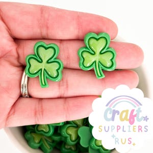 May include: Green shamrock shaped resin embellishments. The shamrocks have a raised, glossy finish.