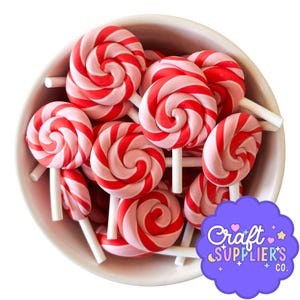 Puede incluir: Un cuenco blanco lleno de numerosas piruletas rojas y rosas arremolinadas sobre palitos blancos. Las piruletas están dispuestas en un patrón circular, con algunas parcialmente visibles. La imagen incluye un logotipo púrpura con el texto "Craft SUPPLIER'S CO."