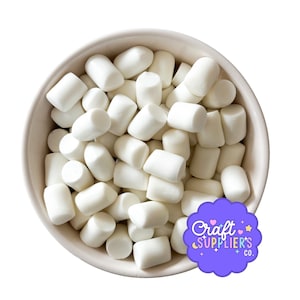 May include: A white ceramic bowl overflowing with white, cylindrical marshmallows. The marshmallows are closely packed together. A purple and white logo for "Craft Supplier's Co." is in the lower right corner.