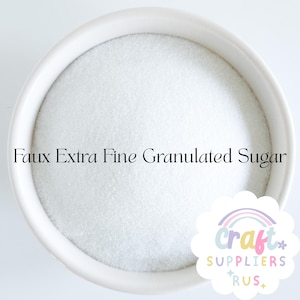 Puede incluir: Un cuenco de cerámica blanco lleno de azúcar granulado extra fino falso. El cuenco es redondo con un borde ligeramente ensanchado. El texto "Faux Extra Fine Granulated Sugar" está impreso en la imagen. Un logotipo de "Craft Suppliers R Us" está en la esquina inferior derecha.