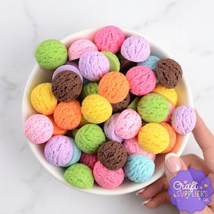 May include: A white bowl filled with colorful, textured ice cream scoops in various colors, including pink, green, yellow, orange, brown, and blue. The scoops are arranged closely together, creating a vibrant and playful display. The image is well-lit, highlighting the details of each scoop.