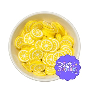 May include: A white bowl filled with numerous small, flat, circular yellow and white lemon slice decorations. Each piece features a radial citrus segment pattern. A purple scalloped label in the corner displays the text Craft SUPPLIER'S CO.