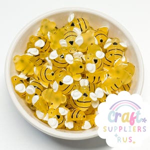 以下が含まれることがあります： 黄色い蜂の形をしたクラフト用品が入った白いボウル。蜂は黒い縞模様と白いアクセントがあります。ボウルは白い背景にあります。Craft Suppliers Rusのロゴが右下にあります。