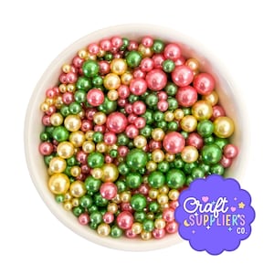 May include: A white bowl brimming with colourful, round sprinkles. The sprinkles are in shades of pink, green, and yellow. A purple logo with the text "Craft Supplier's Co." is also visible.