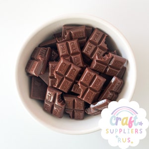 Puede incluir: Un tazón blanco lleno de mini barritas de chocolate. Las barritas de chocolate son todas marrones y tienen la palabra "MILK" impresa en ellas.