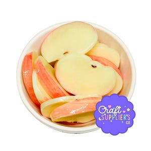 May include: A white bowl filled with multiple sliced apple pieces, each featuring a pale yellow interior and a reddish-pink skin. A purple scalloped label in the bottom right corner displays the white text Craft SUPPLIER'S CO. with small stars.
