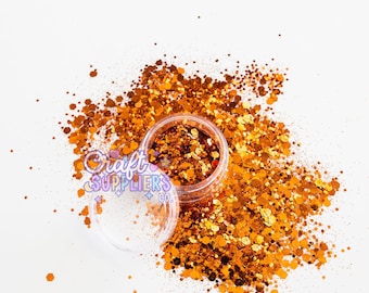 Könnte beinhalten: Ein klarer Plastikbehälter gefüllt mit orangefarbenem und goldenem Glitzer, mit offenem Deckel und verstreutem Glitzer darum. Der Glitzer ist in verschiedenen Formen und Größen. Der Text "Craft Suppliers Co." ist auf dem Behälter zu sehen.