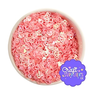 May include: A white bowl filled with pink heart-shaped confetti. The confetti has a pearlescent sheen, creating a shimmering effect. A purple logo with the text "Craft Supplier's Co." is in the bottom right corner. Ideal for craft projects.