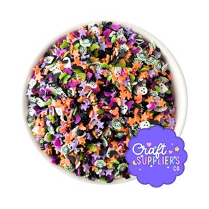 May include: A white bowl filled with colorful Halloween-themed sprinkles. The sprinkles include stars, bats, ghosts, and other shapes in orange, purple, black, green, and white. A purple logo with the text "Craft Supplier's Co." is in the bottom right corner.
