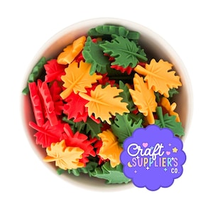 May include: A white bowl filled with colorful leaf-shaped sprinkles. The sprinkles are in shades of red, yellow, and green. A purple sticker with the text "Craft Supplier's Co." is in the bottom right corner.